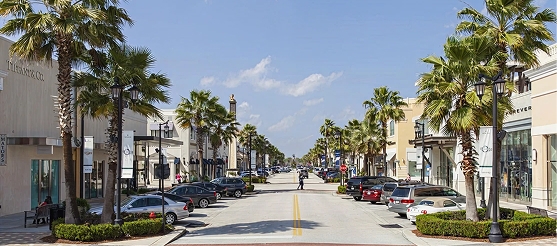 Palm-lined shopping street at St. Johns Town Center in Jacksonville, Florida with parked cars and retail stores.